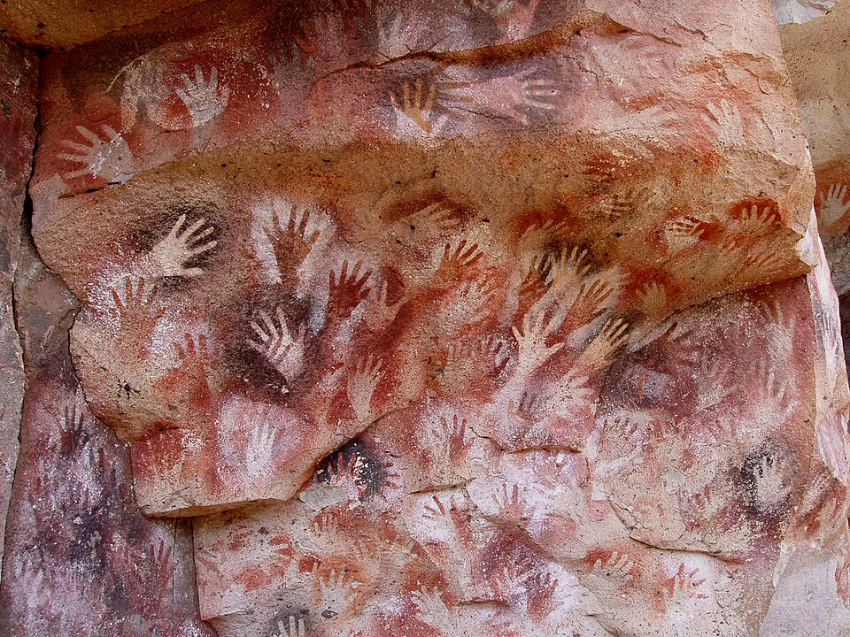 Negative hand stencils in red, black, and ochre covering a cave wall at Cueva de las Manos, Argentina