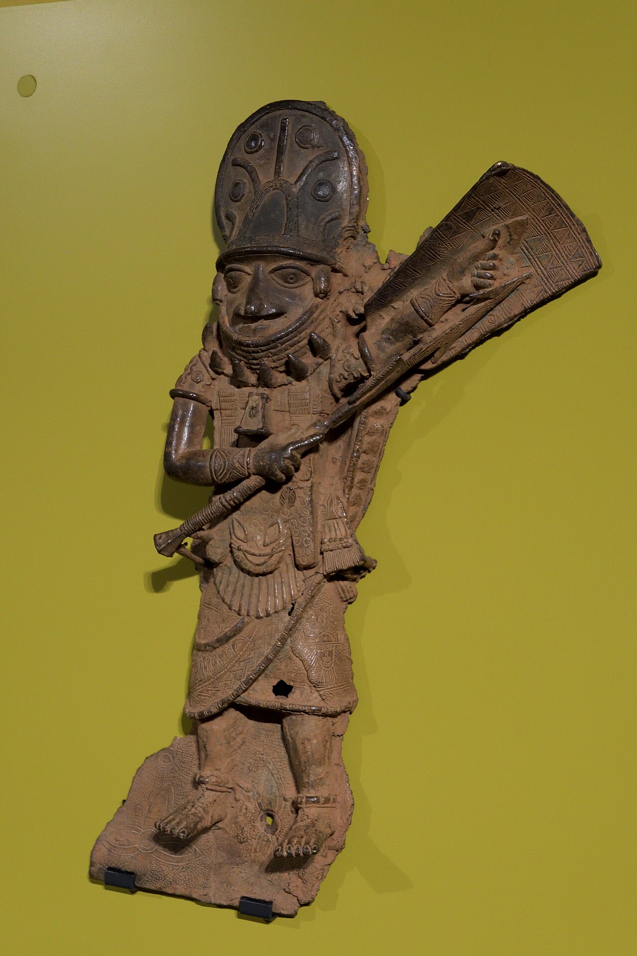 A detailed bronze plaque from the Kingdom of Benin depicting a warrior figure with elaborate regalia