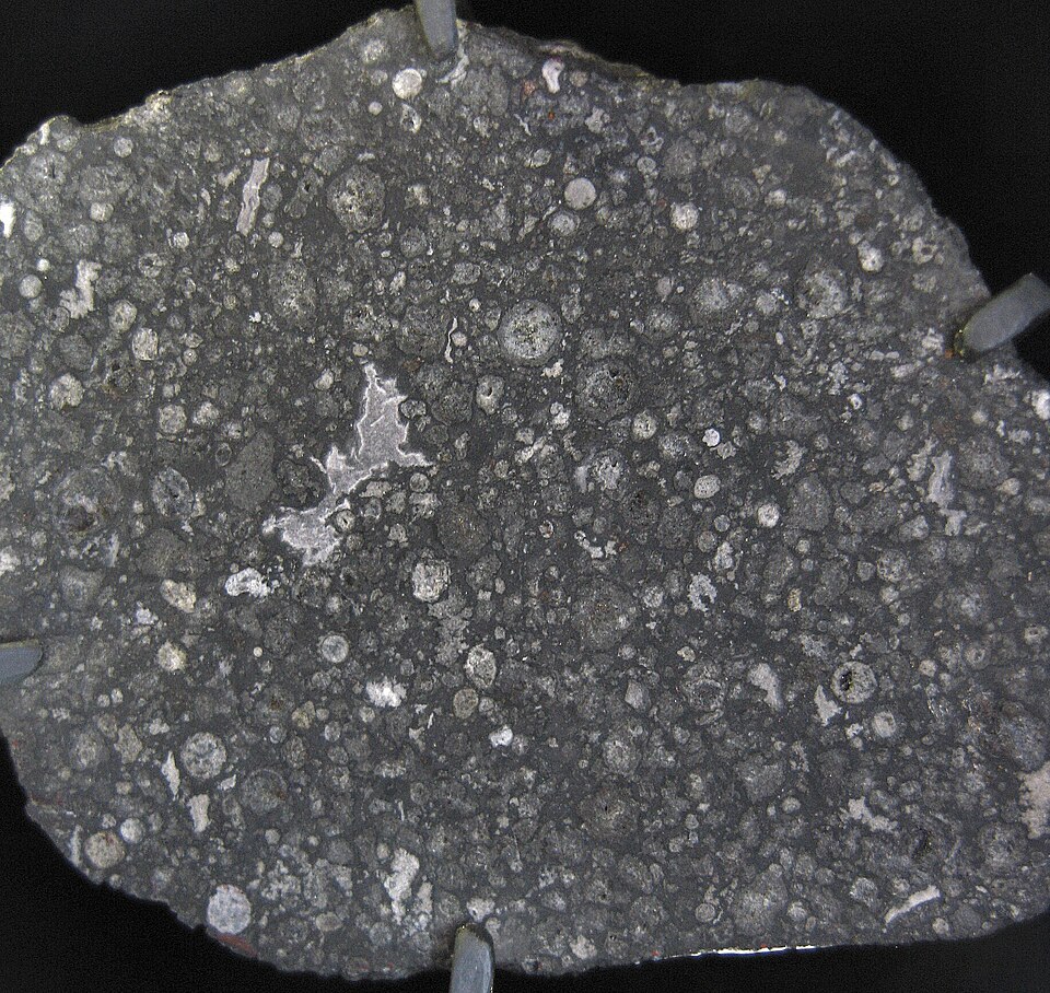 The Allende carbonaceous chondrite meteorite, showing a dark fusion crust and lighter interior with visible chondrules and calcium-aluminium-rich inclusions