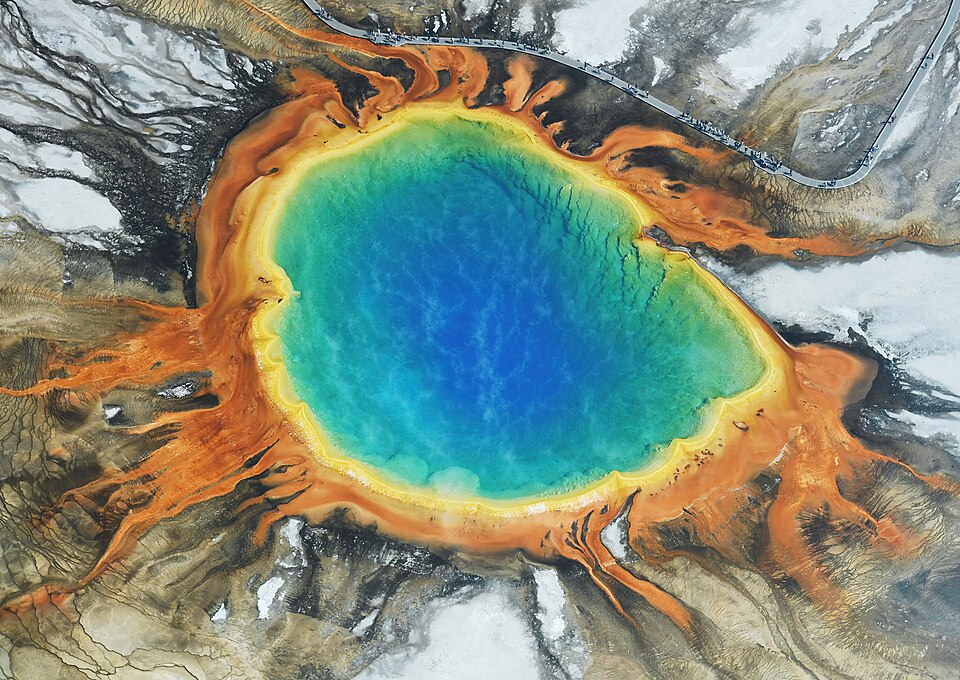 Aerial view of Grand Prismatic Spring in Yellowstone National Park, showing concentric blue, green, yellow, and orange rings around a deep blue central pool